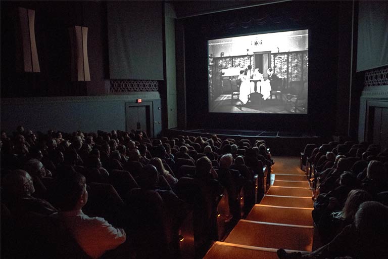 An audience watches a black and white film.