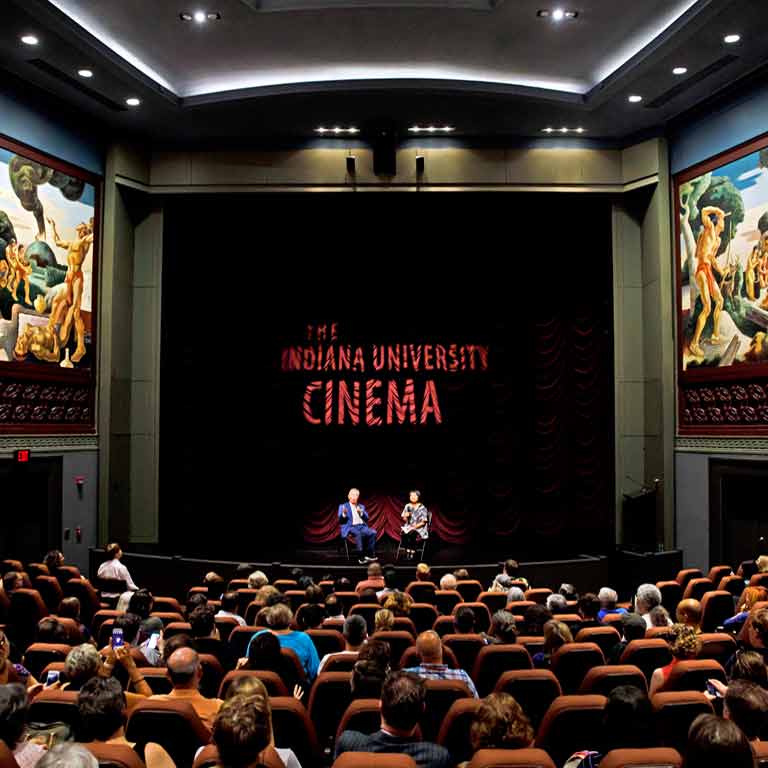An audience listens to an interview. The words 'The Indiana University Cinema' are projected on the curtain.
