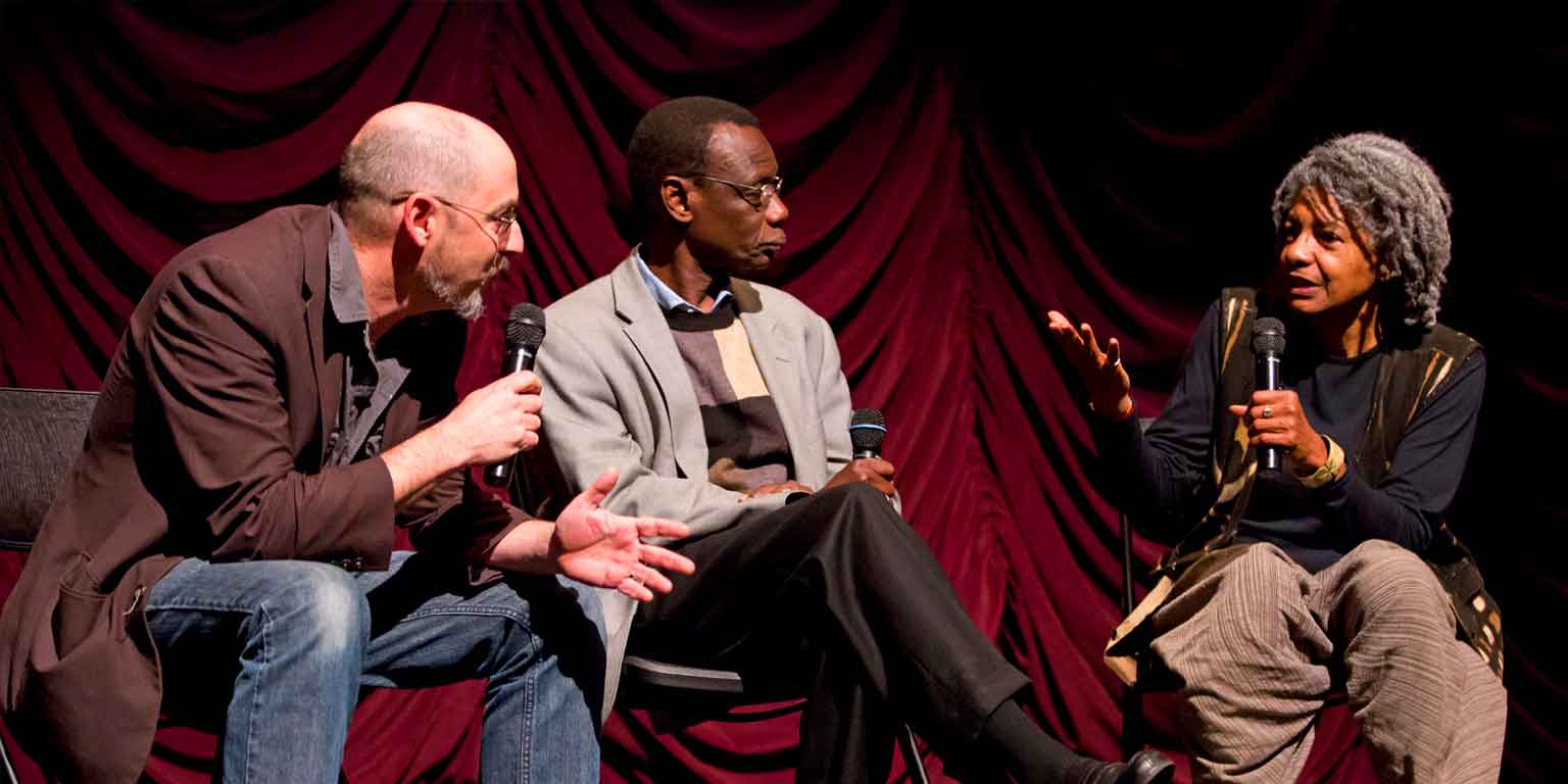 Three people speak before an audience.