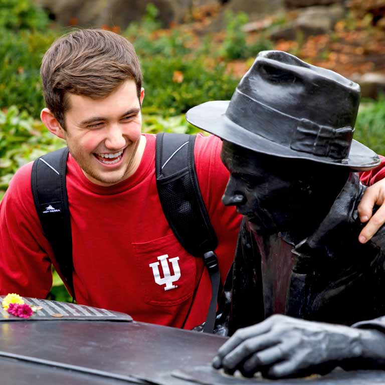 A student puts his arm around a bronze statue.